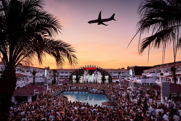 Ushuaïa Ibiza pool at sunset with palm trees and a plane flying over